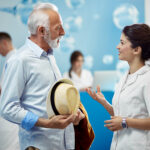 Smiling senior man communicating with a nurse while standing in a lobby at medical clinic.